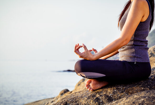 The woman meditating in a yoga pose on the tropical beach. Female meditating overlooking the beautiful sunrise. Healthy mind body and spirit concept.