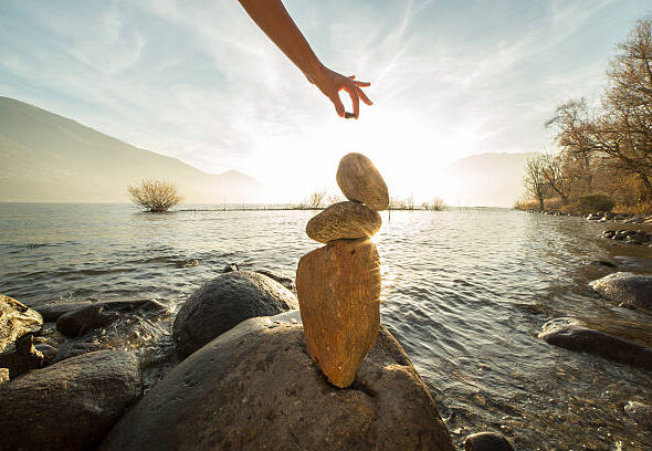 Detail of person stacking rocks by the lake. Sunset time, sunbeam.